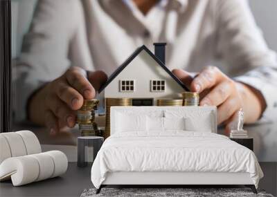 A pair of hands holding a stack of coins with a model of a house, representing the concept of investment real estate Wall mural