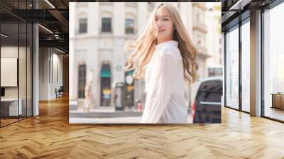 Asian beautiful woman with bronze hair turn s around in white shirt while walks on street. Wall mural