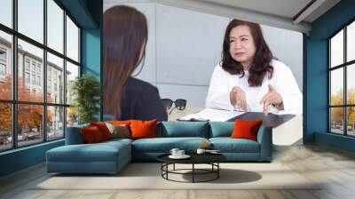 Asian business woman is talking with co-worker woman about work’s problem solution and consulting direction of work in working place. Wall mural