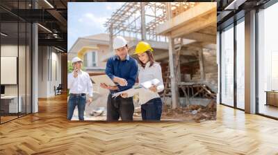 2 male engineers and an Asian female engineer Checking project on laptop with blueprints Standing at a large architectural and industrial construction site Wear helmets and uniforms. Wall mural