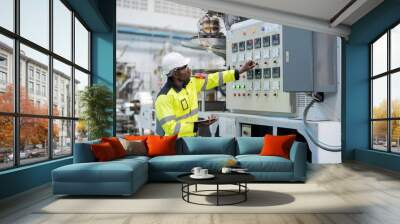 american engineer Hand adjusting a switch on the production control board of a machine. in the plastic and steel industry He is holding a tablet Wear uniforms and helmets. Wall mural