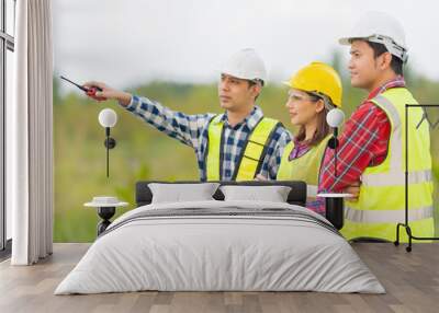 Group photo of a team of 3 Asian male and female engineers with a technician manager wearing a vest, walkie-talkie and helmet working together using a tablet. point to destination Plan future industry Wall mural