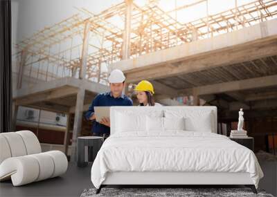 Two asian male and female engineers working together on a tablet and holding blueprints. In construction design about architecture For future industries, wear vests and helmets. Wall mural