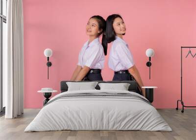 With a charming pink background, the studio photo features two Asian school girls who exude confidence in their high school uniforms, their joyful expressions capturing the essence of their youth. Wall mural