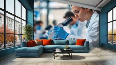 Female scientist in a laboratory looking through a microscope, conducting research and experiments in a modern scientific environment. Wall mural