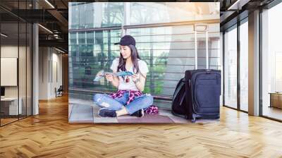 A young woman sitting on the floor of an airport terminal, reading a map beside her luggage. The image captures a moment of planning and exploration, ideal for travel and adventure themes. Wall mural