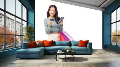 Beautiful Asian woman carrying shopping bags with using credit card and mobile phone standing over isolated on white background Smiling young girl purchasing online through phone using credit card Wall mural