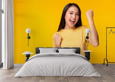 Excited young asian female with raised hands celebrating success. Portrait cheerful positive asian woman with raised fists. Attractive girl get happy, enjoy life yellow background, copy space Wall mural