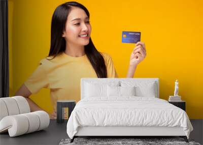 Portrait lovely young asian woman showing plastic credit card and looking at credit card, standing over yellow background. Beautiful girl get satisfied of credit card service with smile on face Wall mural