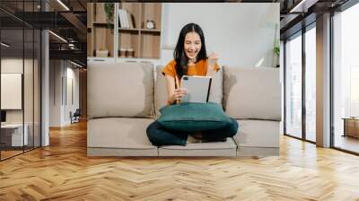 Asian woman using the smartphone and tablet on the sofa at home. Wall mural