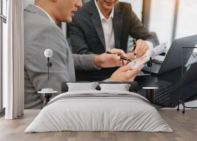 Business documents on office table with smart phone and laptop and two colleagues discussing data in the background in morning light Wall mural