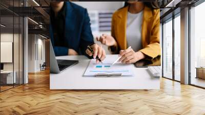 Business documents on office table with smart phone and laptop and two colleagues discussing data in the background in morning light Wall mural