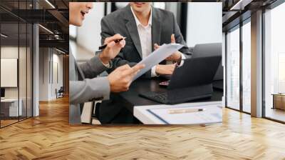 Business documents on office table with smart phone and laptop and two colleagues discussing data in the background in morning light Wall mural