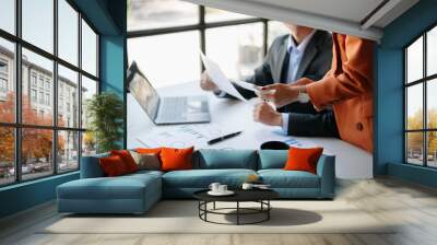 Business documents on office table with smart phone and laptop and two colleagues discussing data in the background Wall mural