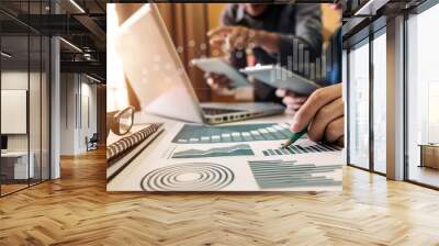 Businessman hand using laptop and tablet with social network diagram and two colleagues discussing data on desk as concept in morning light. Wall mural