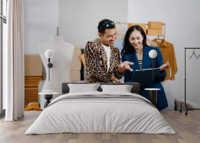 Couple of fashion designers working with fabric and clothing sketches at the studio full of tailoring tools and holds tablet and laptop. Wall mural