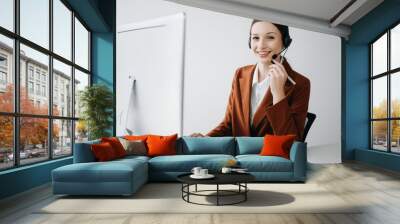 Serious call center operator in wireless headset talking with customer, woman in headphones with microphone consulting client on phone in customer support service in office center.. Wall mural