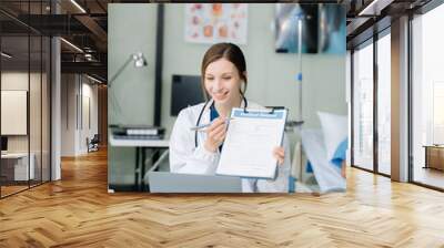 Young female doctor in white medical uniform using laptop and tablet talking video conference call at desk,Doctor sitting at desk Wall mural