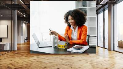 Young real estate agent worker working with laptop and tablet at table in office and small house beside it.. Wall mural