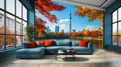 A serene view of Tokyo's iconic Skytree tower against a backdrop of golden and red autumn foliage, with a clear blue sky. Tourists admire the scene from a nearby park Wall mural