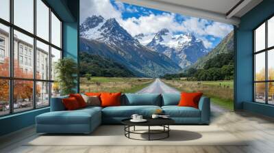 A straight road leading through an alpine valley, framed by towering snow-capped mountains and lush green meadows. Wall mural