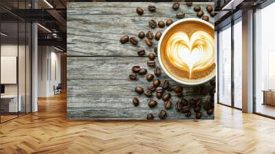 An overhead shot of a latte with intricate heart-shaped latte art, surrounded by scattered coffee beans on a worn wooden background, with space for text Wall mural