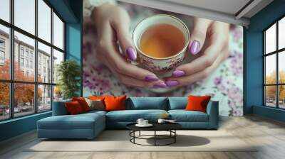 Elegant female hands with purple nails holding a delicate tea cup, vintage setting with floral background and soft tones Wall mural