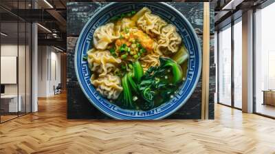 Top view of a bowl of wonton noodles with dumplings, bok choy, and green onions in a clear broth. Wall mural