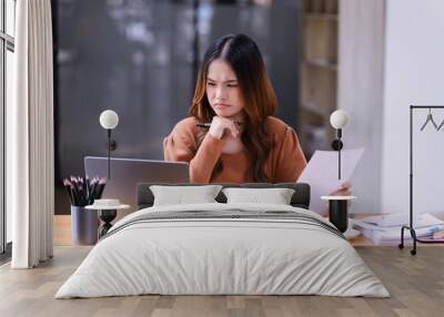 A young woman sitting at working desk in front of a laptop in the office. Wall mural