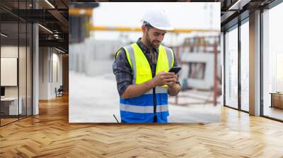 building and construction worker using mobile phone, Hiapanic latin male wearing safety hard hat helmet standing with arms crossed at construction site and looking at camera Wall mural