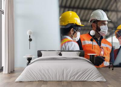 Engineers people are brainstorming solving problems of heavy industrial machinery. Worker man and asian woman wearing face mask prevent covid-19 virus and protective hard hat. . Wall mural