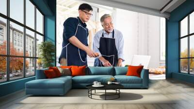 Happy Asian family. Elderly Asian father and Adult son cooking in the kitchen. Indoors at home. Wall mural