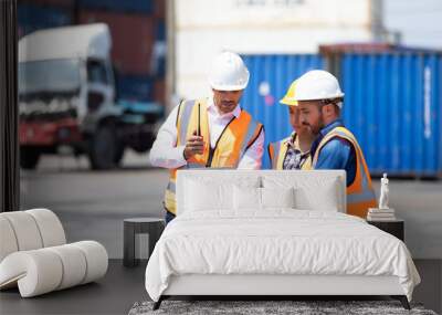 Hispanic man harbor worker talking on the walkie-talkie radio and control loading containers at container warehouse. container yard port of import and export goods Wall mural