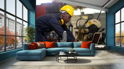 Manufacturing Factory black male Mechanical Engineer Works on Personal Computer at Metal lathe industrial manufacturing factory. Engineer Operating lathe Machinery. American African people. Wall mural