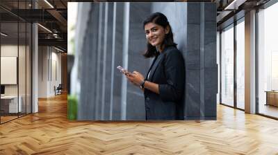 Mobile phone technology lifestyle - Portrait Smiling Young Businesswoman in black suit using smartphone at outside modern office building Wall mural