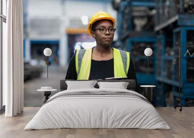 Plus size black female worker wearing safety hard hat helmet inspecting old car parts stock while working in automobile large warehouse Wall mural