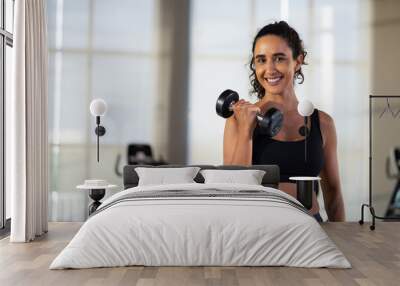 portrait femal lifting dumbbells at gym. beautiful young hispanic woman wearing sporty fitness clothes doing exercise indoors at gym fitness sport club, body and health care Wall mural