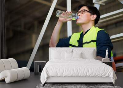 Time for a tea break concept. Asian male warehouse Industrial, factory and energy engineer Specialist drinking water sitting on stair at warehouse office factory workplace. Wall mural