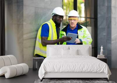 Two engineers African american engineer and caucasian electrician wearing white hard hat walk in new building holding solar panel on hand and Discuss Work Wall mural