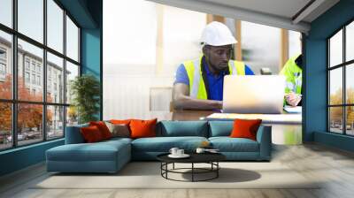 Two engineers African american engineer and caucasian electrician wearing white hard hat working on laptop computer at workplace office. clean and green alternative energy concept. Wall mural