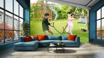 Young Asian couples are pretending to spray water on each other with a hose at home. Happy family concept. Smiling couple in love outdoors Wall mural