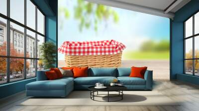 Straw empty basket decorated with picnic checkered cloth  nature background. Wall mural