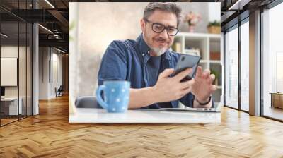 50s man checking news on phone at home. Confident happy smiling. Wall mural