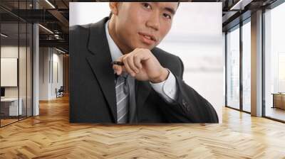 Confident young asian businessman sitting at desk looking at camera. Wall mural