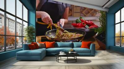 Woman cooking frying chicken meat in wok pan on kitchen table. Closeup hands. Cosy dark room. Real, authentic cooking.  Wall mural