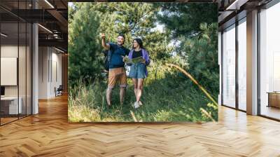 Happy couple tourists with backpacks looking at the map for searching right direction, walking outdoors in the summer forest Wall mural