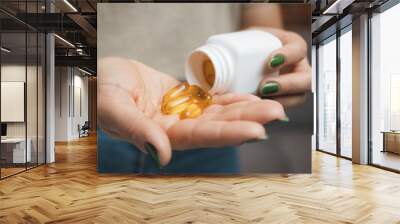 Young woman holds omega 3 capsules in a hand, female take fish oil supplements and vitamins from a bottle, close-up view Wall mural