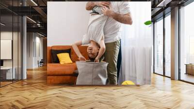 Father and son have fun at home, boy upside down. Wall mural