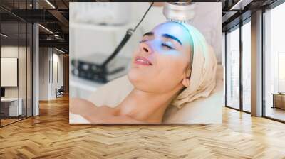 young healthy woman with good skin doing cosmetic procedures in spa clinic. light treatment. Wall mural