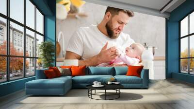 Young man siting and feeding baby girl Wall mural